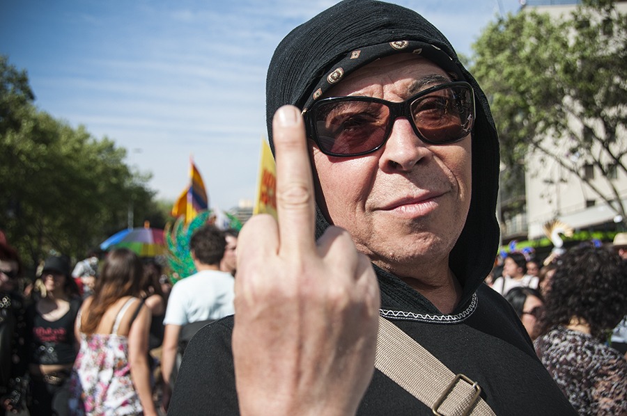 Pedro Lemebel con gorro negro y gafas de sol, levantando el dedo medio ante la cámara.