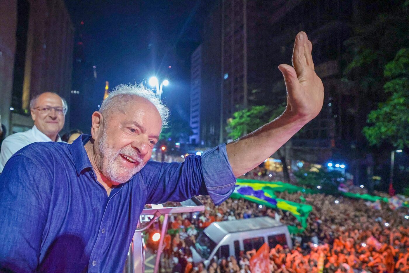 Lula sonríe y saluda con la mano en alto a una multitud de noche en São Paulo.
