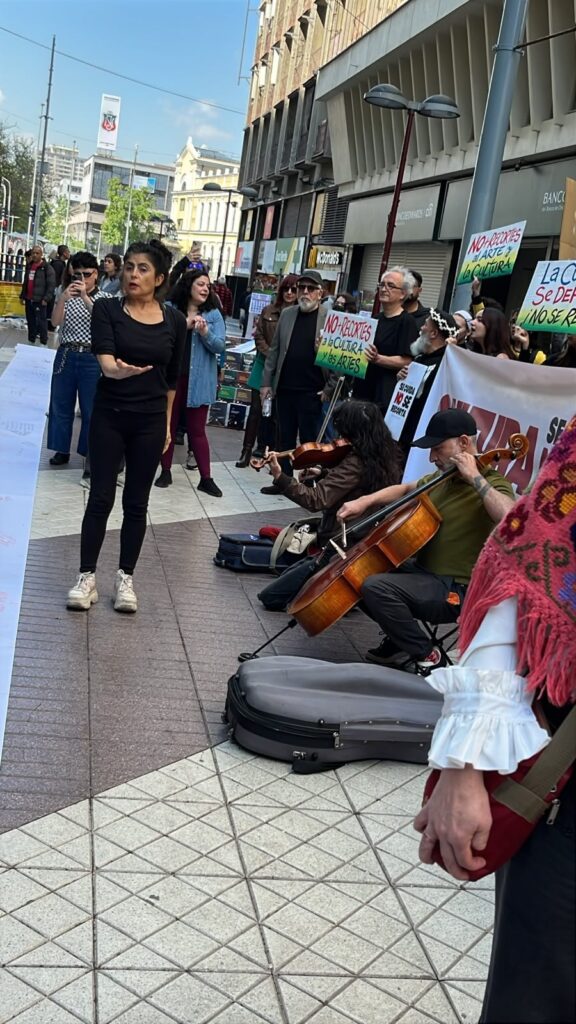 Una mujer interviene frente a músicos que tocan violín y violonchelo en Paseo Ahumada, rodeados de manifestantes con carteles